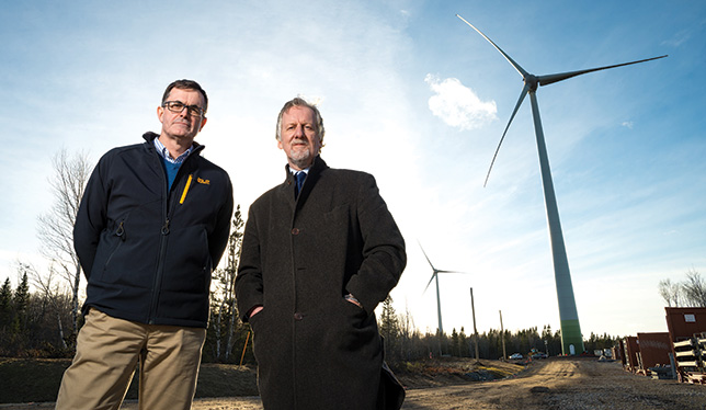 The wind turbines rise up behind Donnie MacIsaac, director of facilities management at CBU, and president David Wheeler. Photo courtesy of Cape Breton University.