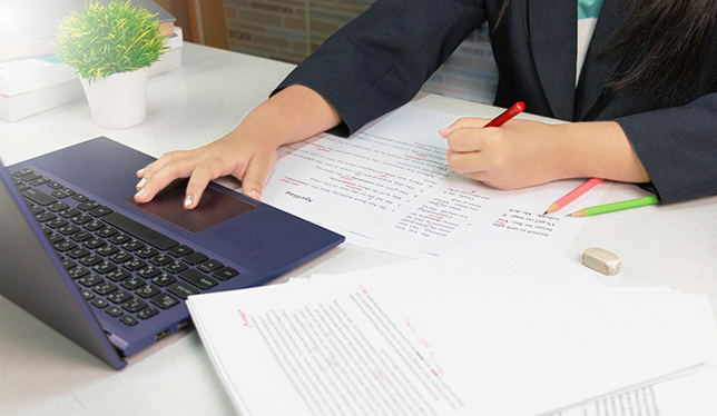 hand holding red pen over proofreading paper on white table