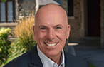 A bald man smiling at the camera wearing a suit jacket and shirt.