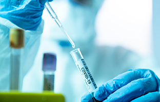 Close up photo of female scientist holding a laboratory pipette and a blood sample tube for covid-19 in laboratory. She is wearing a protective suit, laboratory glasses, surgical mask and surgical gloves. Selective focus on tube. Shot with a full frame mirrorless camera.