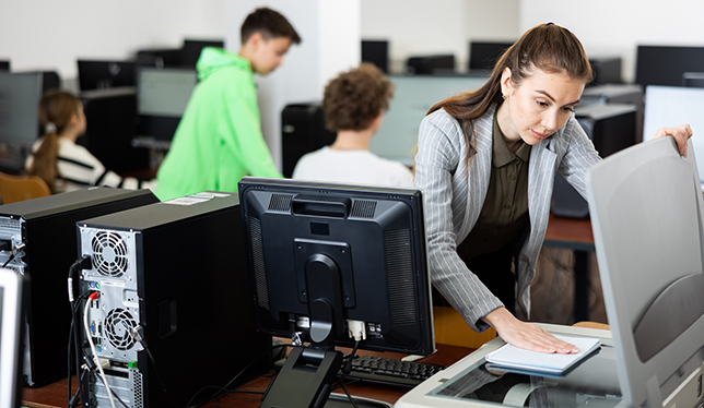 Interested young woman copying notes on copy machine in university library computer lab